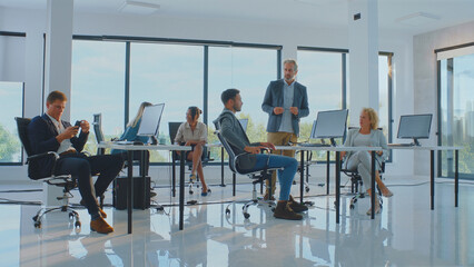 Business colleagues working in a contemporary open-plan office, a senior manager overseeing multiple employees at their individual desks, fostering a collaborative and professional work environment