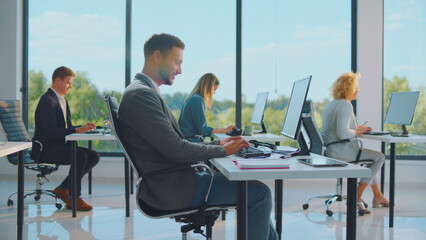 Diverse office workers staying productive at their desks, using computers in a bright, contemporary...