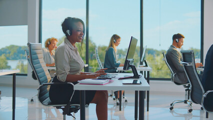 Multiracial team of professional customer service representatives wearing headsets and typing on...