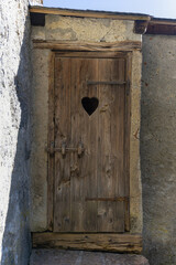 Old wooden door with heart-shaped cutout set in a rustic stone wall under natural daylight