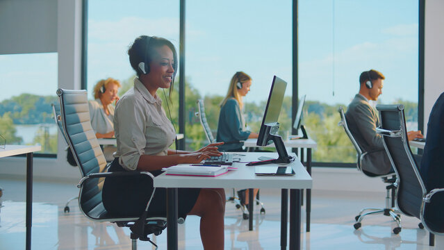 Multiracial team of professional customer service representatives wearing headsets and typing on computers, providing direct assistance and support for clients in a modern office environment