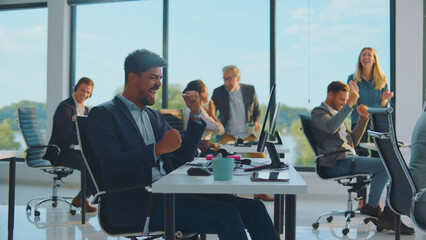 Diverse business professionals in a bright modern office are cheering, raising fists in the air,...