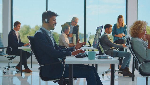 Diverse team of customer service agents wearing headsets and providing online support while collaborating in a bright, contemporary office environment