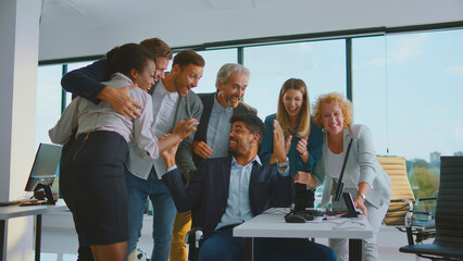 Diverse business professionals cheering and applauding a colleague, acknowledging a significant achievement, celebrating good news and teamwork in a bright contemporary office environment