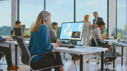 Young businesswoman wearing a headset and smiling, making a video call on her computer with a map...