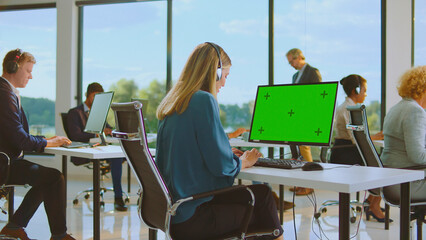 Employees wearing headsets and typing on computers in a bright, modern call center office, focusing on providing customer service and technical support