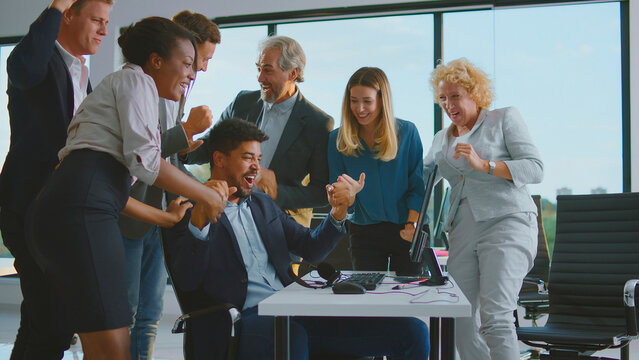 Happy business team members cheering with excitement and triumph around a computer, celebrating a significant achievement or project success in a modern office environment