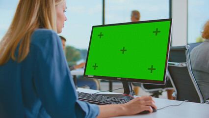 Woman employee using a personalized computer screen with a green screen mock-up, working in an office with natural light, focusing on digital tasks and presentations