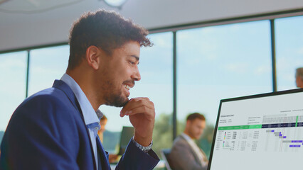Happy business man collaborating in a modern office, watching a gantt chart on a desktop computer screen, successfully managing a complex corporate project