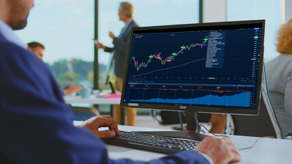 Business professional monitoring financial data on a computer screen, analyzing stock charts and graphs in a modern office environment focused on investment and trade