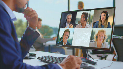 Business professional engaging in a virtual video meeting with diverse colleagues on a desktop computer, collaborating and communicating remotely from an office environment