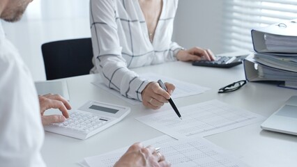Professional women collaborating, reviewing financial reports using calculator, laptop, discussing...