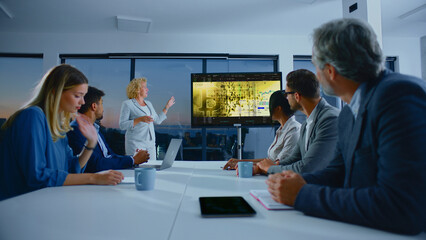 Business executive presenting a bitcoin and cryptocurrency market analysis on a large screen to a diverse team of colleagues in a modern office meeting room