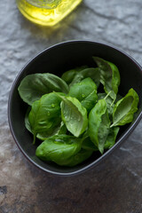 Fresh green basil leaves in a bowl, vertical shot on a dark-grey granite background, selective focus