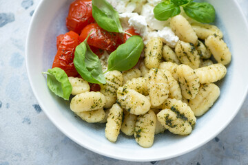 Italian gnocchi with basil oil, roasted tomatoes, ricotta cheese and fresh green basil, horizontal shot, middle close-up