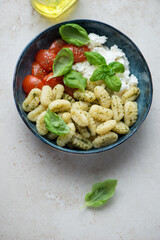 Bowl of potato gnocchi with ricotta, roasted tomatoes and basil, vertical shot on a light-beige stone surface, high angle view