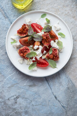Plate of tomato, cottage cheese and figs salad, vertical shot on a blue and beige stone background with space, high angle view