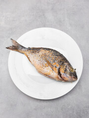 Delicious grilled dorado fish lying on white plate on gray background