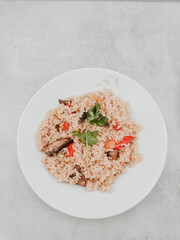Delicious brown rice dish with mushrooms, peppers and parsley on white plate