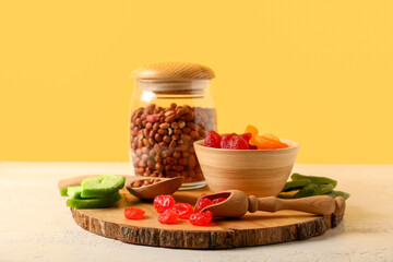 Bowl with different candied fruits and jar of peanuts on white table