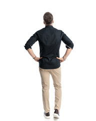 Naklejka premium back view of young casual man holding hands on hips and stepping