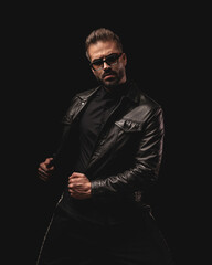 sexy unshaved man with sunglasses looking forward and adjusting jacket