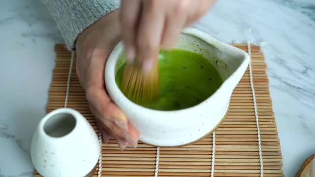 Whisking matcha tea creating rich frothy foam in natural light.