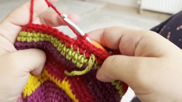 A woman whose face is not visible is knitting with a crochet hook. Handmade idea concept. Hobby, leisure. Hands knitting with colored wool yarn and crochet hook. Horizontal 4k video.