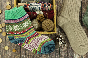 Knitted warm socks for fall and winter. Yarn in a wicker basket and colorful socks on a textured wooden background.