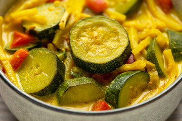 Close-up view of a bowl of the vegan version of Thai yellow curry made of zucchini, red bell pepper, coconut milk, and bamboo shoots. 