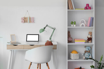 Interior of children's room with bookshelf, different toys and laptop on workplace