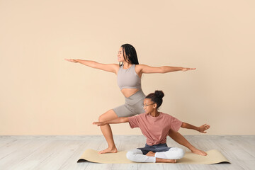 African-American mother with her teenage daughter practicing yoga near beige wall