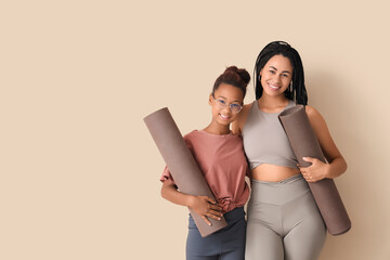 African-American mother with her teenage daughter and yoga mats hugging on beige background