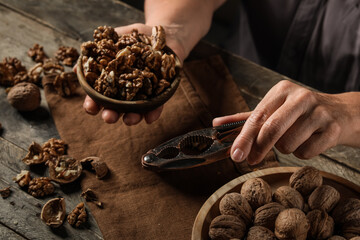 Elderly woman with nutcracker, whole and peeled walnuts at wooden table