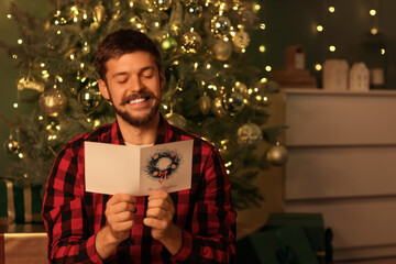 Young man reading Christmas greeting card at home
