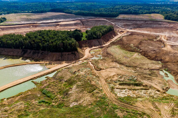 Expansive open-pit sand quarry, showing massive excavation, rugged dirt roads, and mineral-rich water bodies. Distant green forests frame the industrial landscape