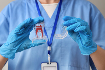 Female dentist with occlusal splint and plastic tooth on grey background, closeup