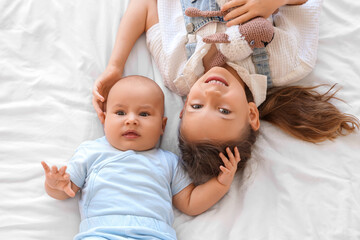 Little girl with toy sheep and her baby brother lying on bed, top view