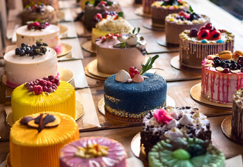 Many cakes are placed on the table next to each other, each cake has a different color and different decoration
