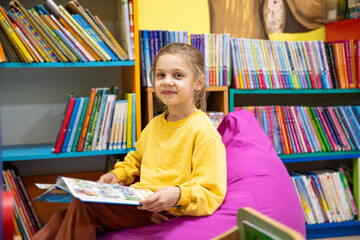 Portrait of a 7-8-year-old blonde girl in a yellow longsleeve in a library with books