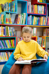 Portrait of a 7-8-year-old blonde girl in a yellow longsleeve in a library with books