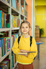 Portrait of a 7-8-year-old blonde girl in a yellow longsleeve in a library with books