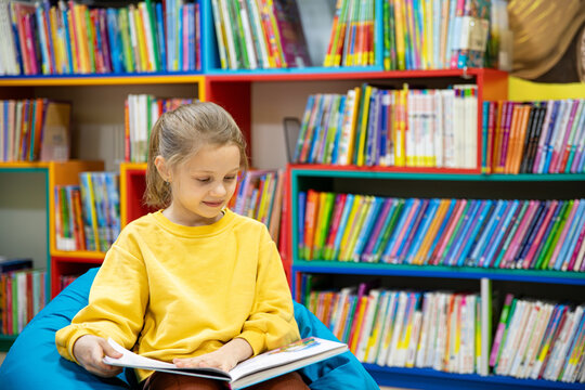 Portrait of a 7-8-year-old blonde girl in a yellow longsleeve in a library with books