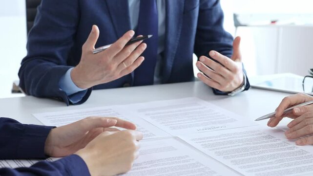 Business people meeting in an office, discussing important documents, pointing to a contract for signature, finalizing a deal, negotiating agreement terms, financial transaction concept