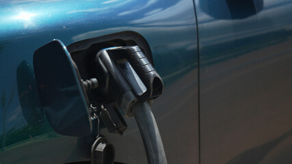 Close-up shot of an electric car's charging socket and plug, showing the process of refueling a modern blue-green EV outdoors, representing renewable energy and the future of electric mobility