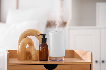 Air humidifier with essential oil and decor on table in bedroom, closeup