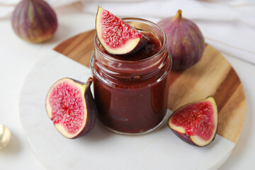 Board with jar of sweet fig jam on marble background