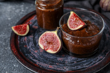 Plate with glass and jar of sweet fig jam on grey grunge background