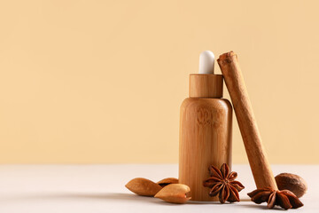 Composition with bottle of essential oil, nuts, cinnamon stick and anise stars on white table near beige wall, closeup