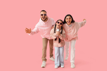 Fototapeta premium Happy family in sunglasses with microphone singing on pink background